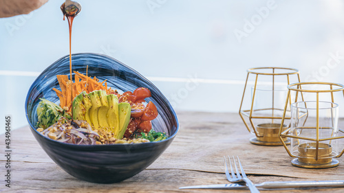 Foto Poke ball ensalada de verdura fresco con aguacate y tomate cherry sobre mesa de madera y fondo desenfocado de océano