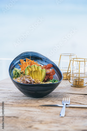 Foto Poke ball ensalada de verdura fresco con aguacate y tomate cherry sobre mesa de madera y fondo desenfocado de océano