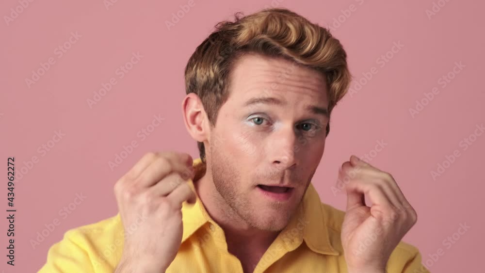 The close-up view of a smiling man with makeup correcting his appearance and standing in a pink studio The close-up view of a smiling man with makeup correcting his appearance and standing in a pink studio