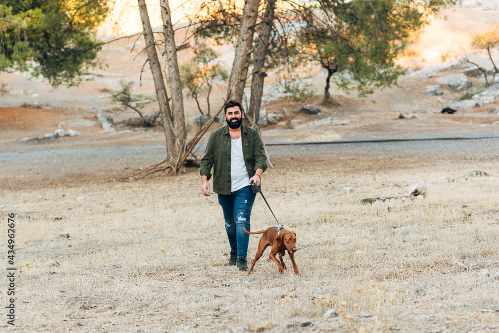 Bearded man walking his dog outside at sunset. 40 year old guy walking with his dog in the countryside. Horizontal photo with copy space Bearded man walking his dog outside at sunset. 40 year old guy walking with his dog in the countryside. Horizontal photo with copy space