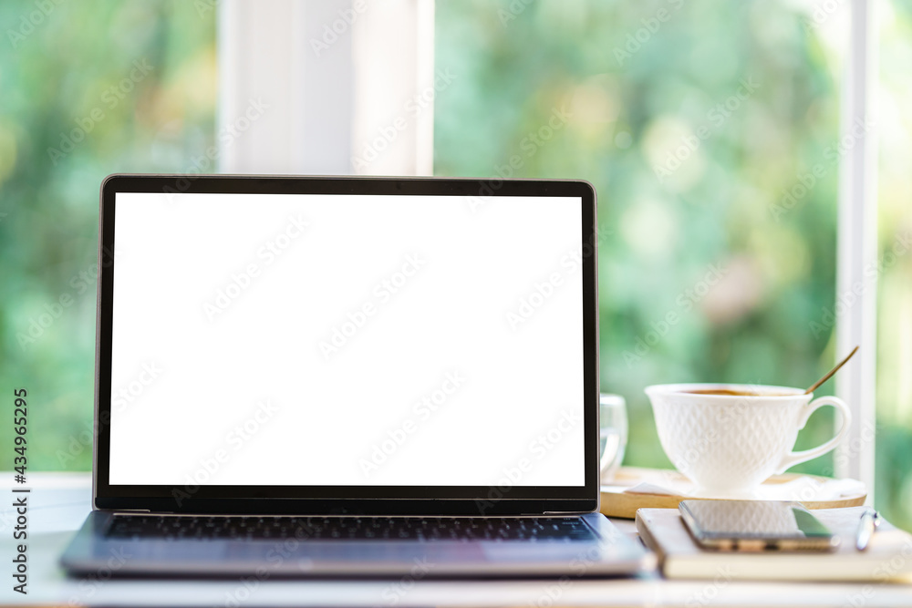 Fototapeta premium Mockup of laptop computer with empty screen with notebook,coffee cup and smartphone on table side the window in the coffee shop at the cafe,White screen