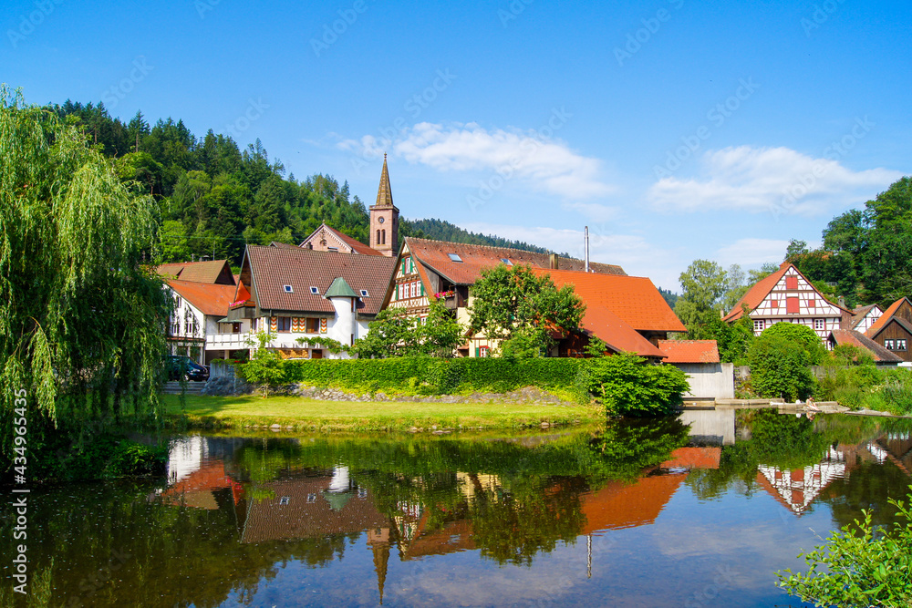 Scenic view of the small medieval village of Schiltach, Germany with its church tower in the center. Beautiful half-timbered houses and weeping willow reflect in the river's water.