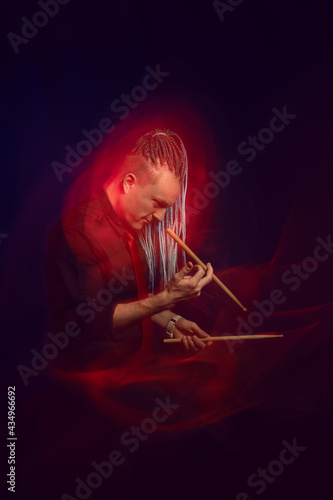 Handsome man with interesting braids on a black background with drumsticks, shot with mixed light