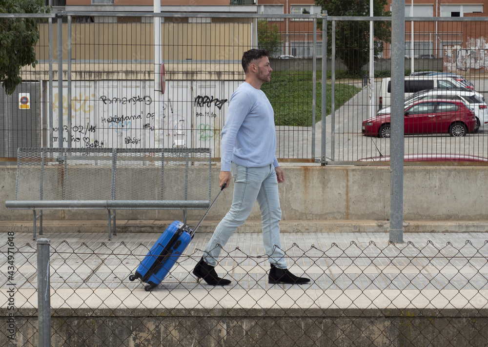 a 40 to 45 year old man walks with a blue suitcase, at the exit of a station.