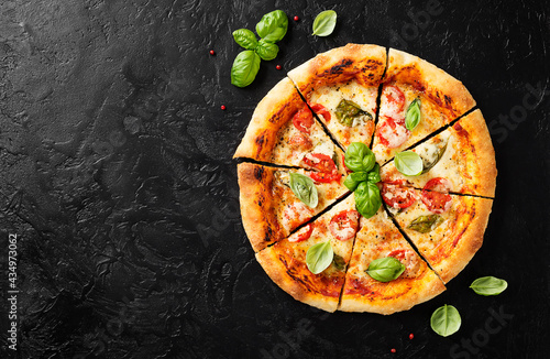 Fresh Homemade Italian Pizza Margherita with mozzarella cheese,cherry tomatoes and fresh basil leaves. Black stone background, top view