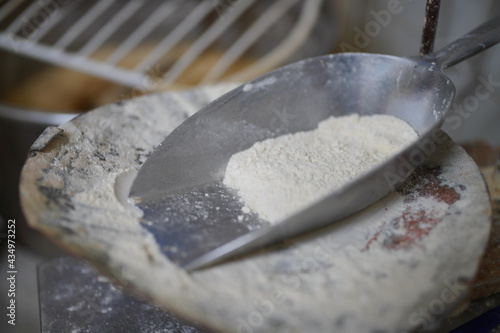 Mehlschaufel mit Mehl Type 550 vor dem Gitter einer Teigmaschine einer Bäckerei während der Arbeit