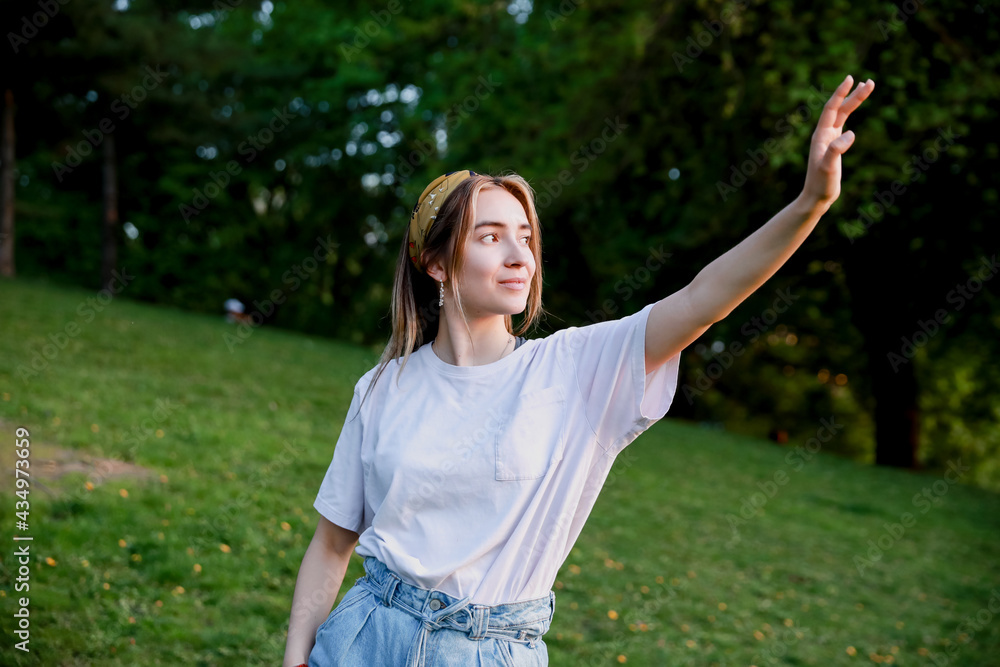 Beautiful European woman wearing jeans and white shirt in the park. Happy girl enjoying the summer with her hand up pointing on the right. Wellness and happiness concept. Beautiful European woman wearing jeans and white shirt in the park. Happy girl enjoying the summer with her hand up pointing on the right. Wellness and happiness concept.