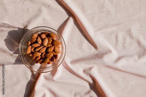 A glass bowl with almonds on a pink textile. Sunlit photo. Copy space for text on the right. 