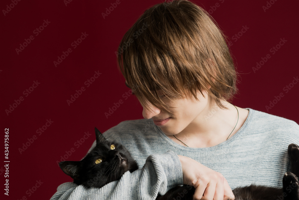 A young guy with long hair holds a cat in his hands A young guy with long hair holds a cat in his hands