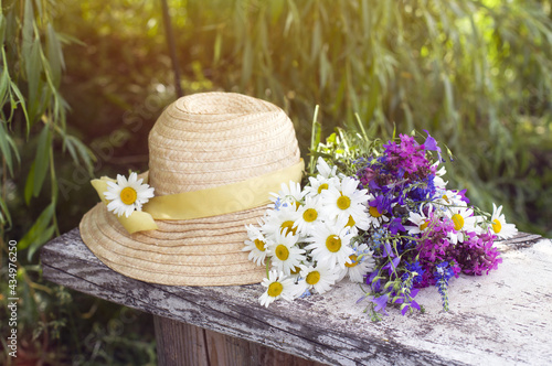 Fototapeta Naklejka Na Ścianę i Meble -  straw hat, a bouquet of white daisies and bright wildflowers on a background of foliage. summer composition.