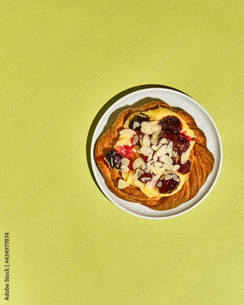 Sweet pastries, a bun with raspberries, almonds and cream on a plate on a colored background in a modern style, top view with space for text Sweet pastries, a bun with raspberries, almonds and cream on a plate on a colored background in a modern style, top view with space for text