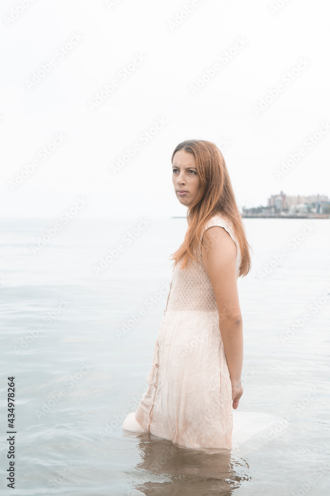 Brooding Latin female in a beige sundress is standing in the water Brooding Latin female in a beige sundress is standing in the water