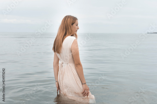 Back view of a Hispanic female in a beige sundress standing in the water