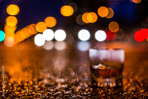 Lights of the city at night through the glass of alcohol, headlights of the approaching cars. View from the glass level with brandy standing on the asphalt, defocused image