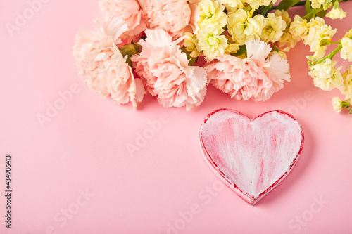 Bouquet of pink carnations and yellow matthiola with decorative heart. Design concept of holiday greeting with carnation bouquet on pink table