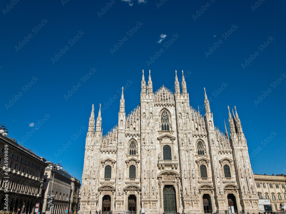 View of the Milan Cathedral and the square. Duomo di Milano. Overview of the facade of the cathedral in white marble. Buttresses, pinnacles and spiers. Statue of the Madonnina. Lombardia. Italy
