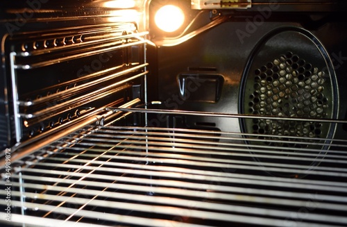 A view of the inside of an empty oven with lighting bulb and a wire rack.
