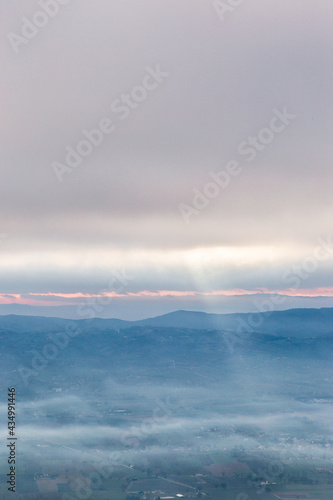 View from above of sunrays coming down on mist between hills and mountains in Umbria valley  Italy