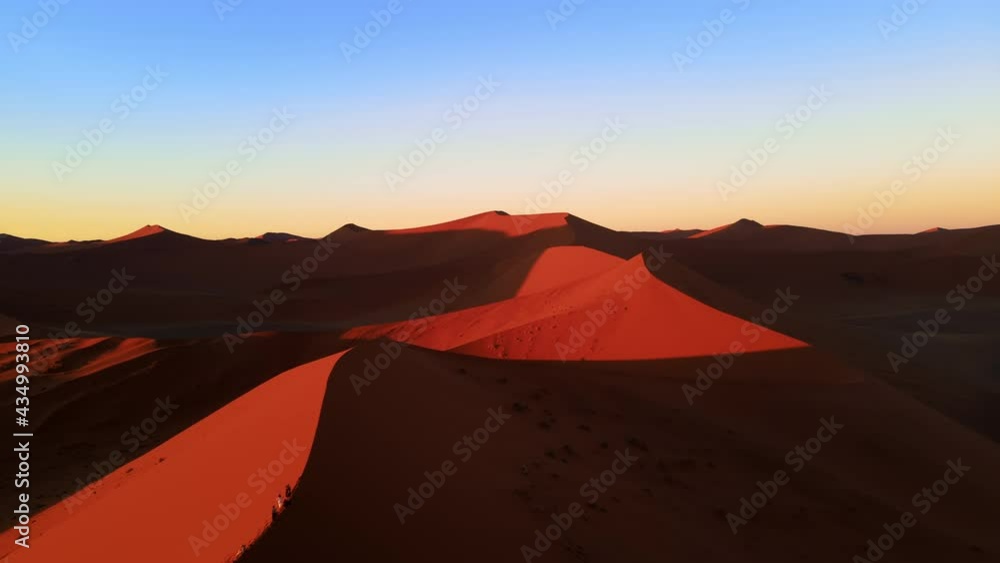 Drone shot from height over massive orange dune in african desert. Amazing aerial view of hill of sand under clear blue dusk sky. Colourful contrast of barren wilderness captured by drone.