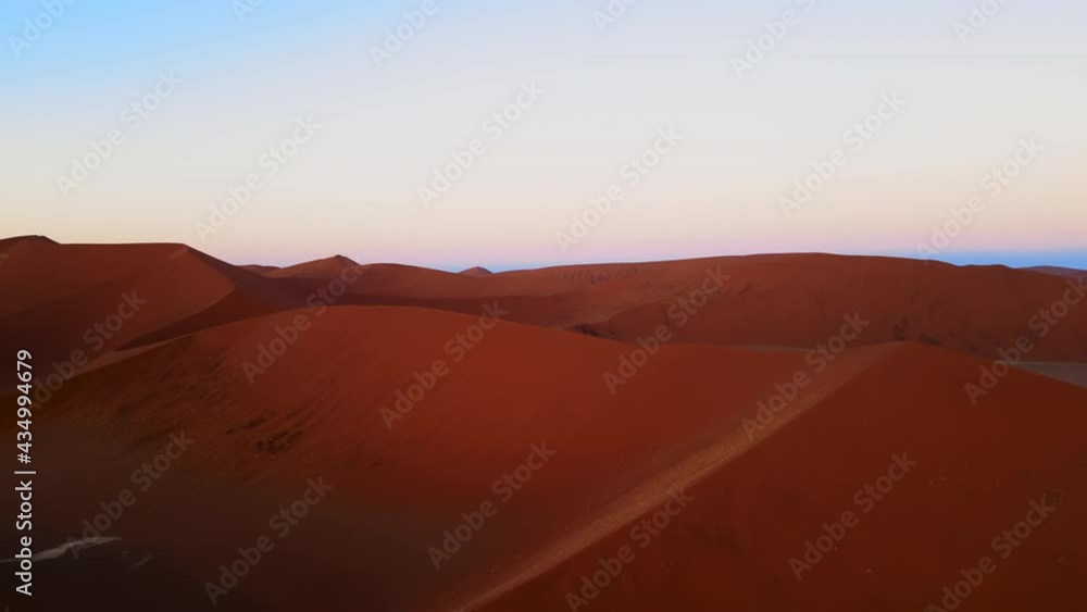 Drone shot of incredible desert landscape in africa. Aerial view of tall colourful dunes in a barren wilderness under clear blue sky at dusk. Bright orange sand hills showing powers of nature shot by Drone shot of incredible desert landscape in africa. Aerial view of tall colourful dunes in a barren wilderness under clear blue sky at dusk. Bright orange sand hills showing powers of nature shot by