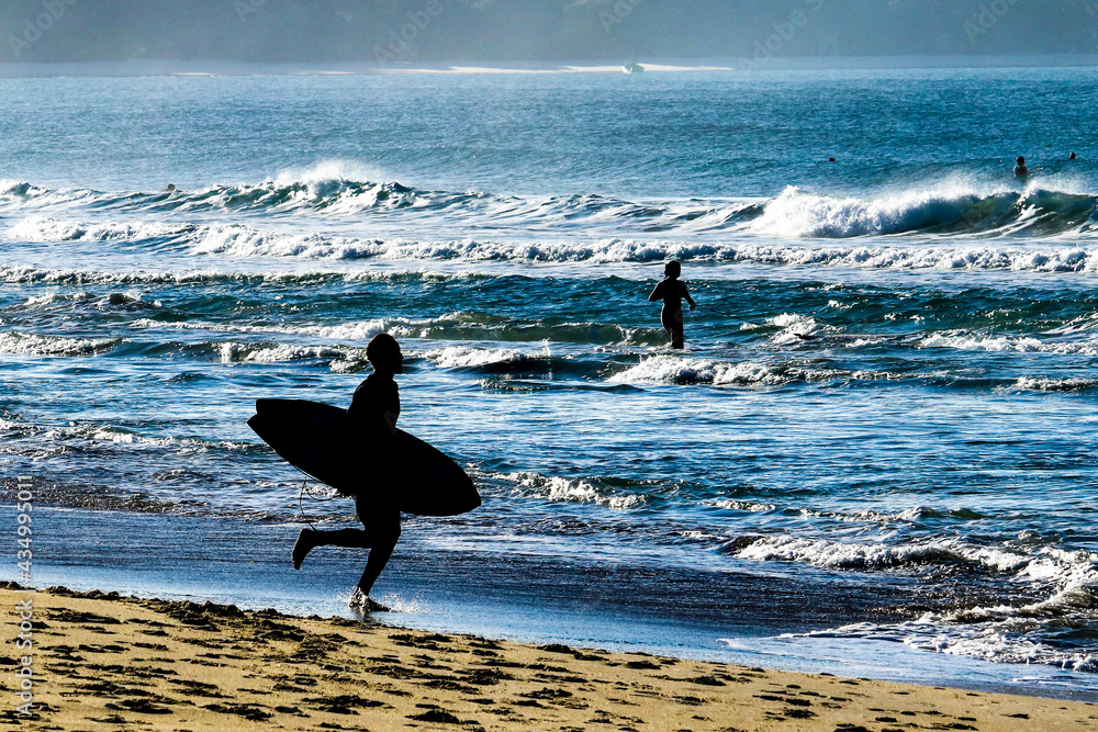 A surfers silhoutte running to the ocean at Campeche beach with campeche island on background