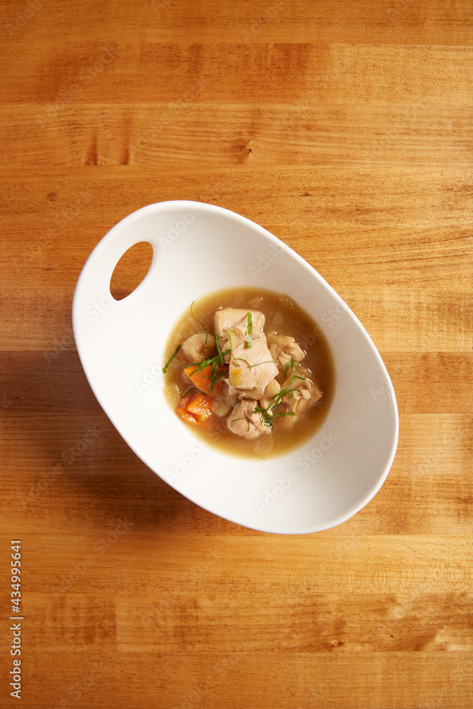 Top view of chicken and vegetable soup served in a white bowl on a wooden surface Top view of chicken and vegetable soup served in a white bowl on a wooden surface