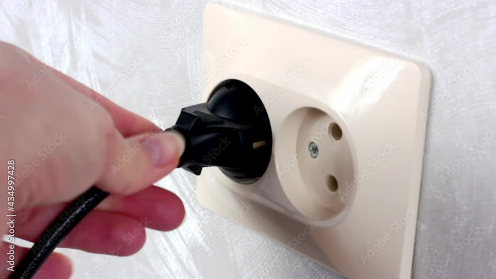 Caucasian woman hands switch on the black power plug into the white electrical socket close up