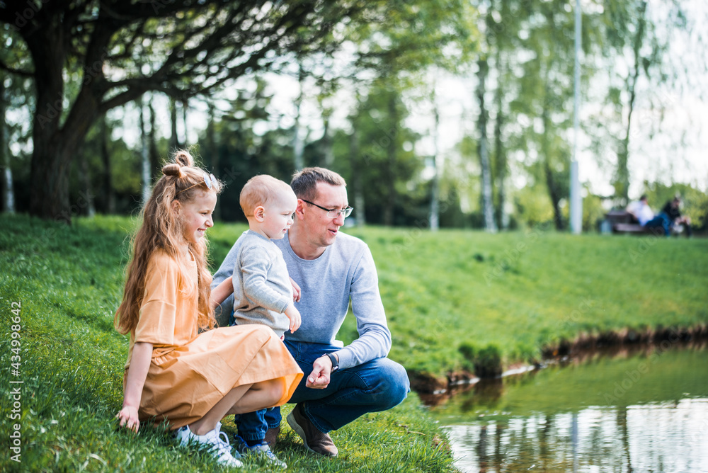 happy family on the bank near the river in summer in the park. Concept of family vacation in nature. dad and kids, father's day happy family on the bank near the river in summer in the park. Concept of family vacation in nature. dad and kids, father's day