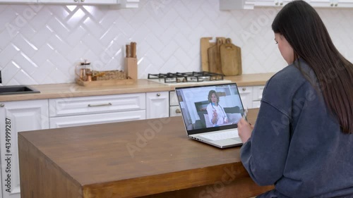 Young woman in homel wear talking by video call with cheerful female doctor therapist while staying at home, patient explaining symptoms through video conference on laptop. Telemedicine concept photo