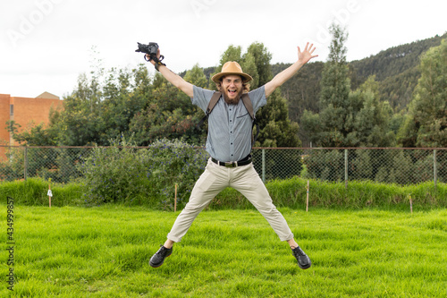 young man photographer and traveler jumping in nature holding camera in his left hand with hands and legs stretched out and smiling.