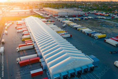 Logistics park with warehouse and loading hub. Semi-trailers trucks stand at ramps and wait for load and unload goods. Aerial view at sunset photo