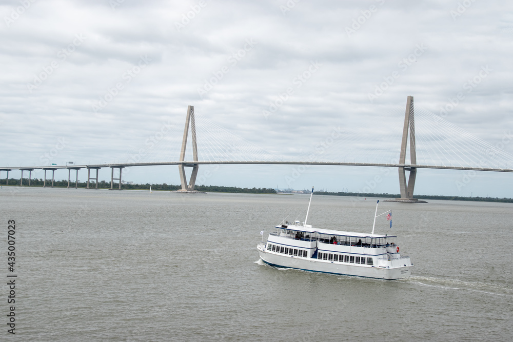 Fototapeta premium A tour boat on the the Cooper River in front of the Ravenel Bridge in Charleston, South Carolina during a cloudy day
