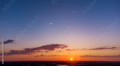 Beautiful, tropical Florida sunset with the moon and a jet with contrails.