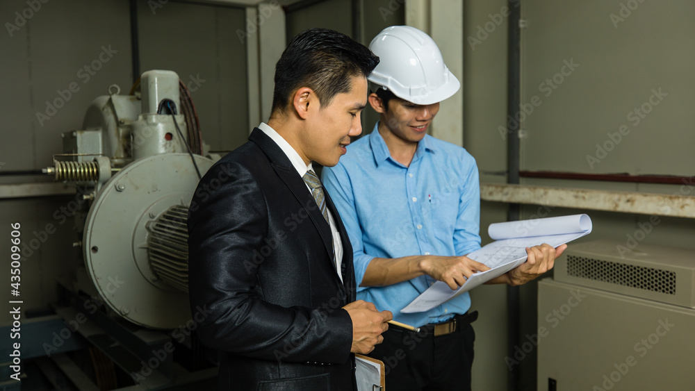 Asian businessman boss wearing black suit standing and discussing with young engineer in elevator machine port. Concept for brainstorming, review, and inspecting workplace. Asian businessman boss wearing black suit standing and discussing with young engineer in elevator machine port. Concept for brainstorming, review, and inspecting workplace.