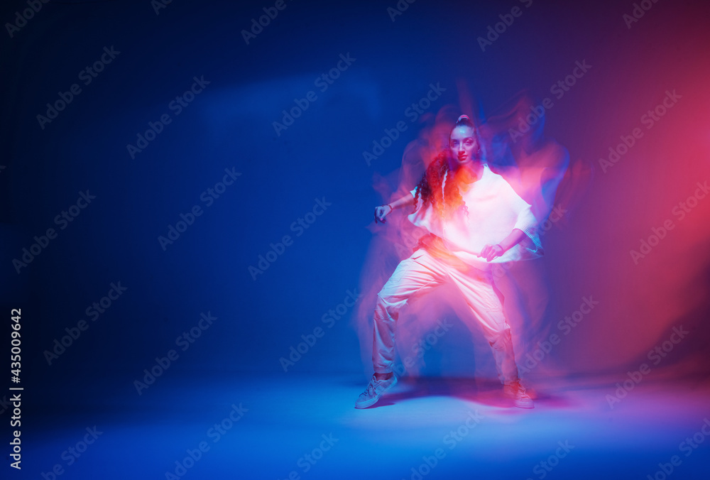 Stylish dancing modern girl moving in colorful neon studio light. Long exposure. Copy space