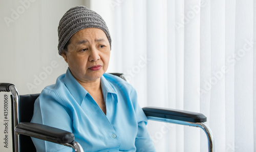Older Asian woman patient covered the head with clothes effect from chemo treatment in cancer cure process lonely sitting on wheelchair and wait for someone to visit her