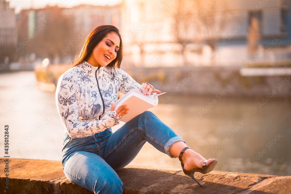 A brunette Latin girl in the city at sunset by the river having fun reading a book. A brunette Latin girl in the city at sunset by the river having fun reading a book.