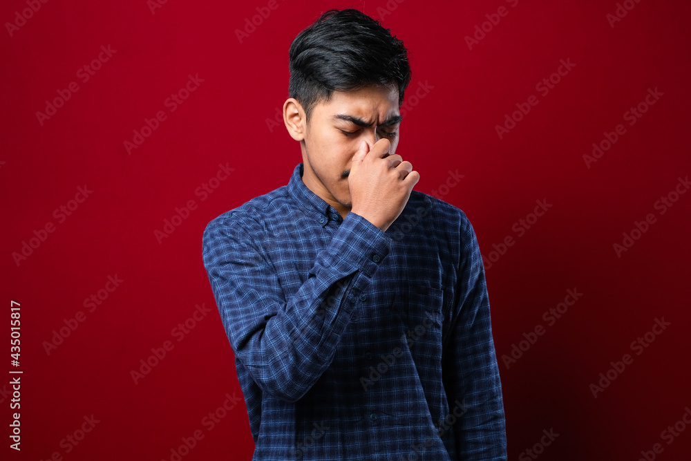 Young handsome asian man wearing casual shirt standing with hand on head for pain in head because stress. Suffering migraine. Young handsome asian man wearing casual shirt standing with hand on head for pain in head because stress. Suffering migraine.