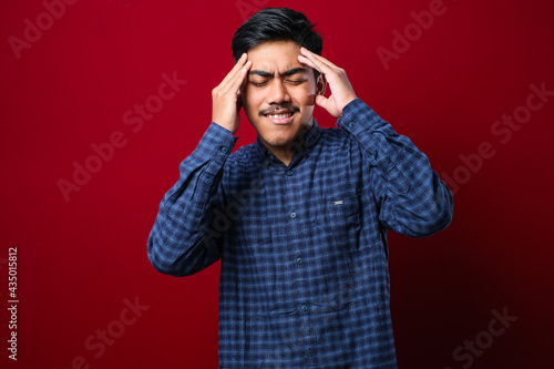 Young handsome asian man wearing casual shirt standing with hand on head for pain in head because stress. Suffering migraine. © Reza