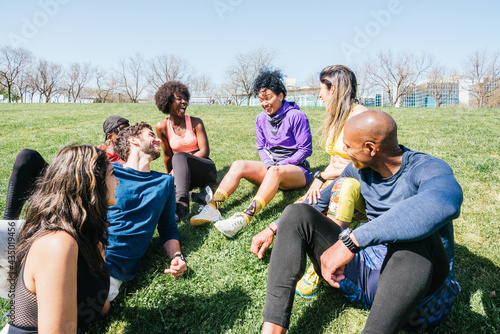 Group of runners in a park lying on the grass. Talking and laughing.