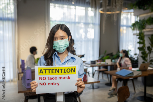 woman asian wearing a surgical mask puts an open sign warning "No Mask No Entry",