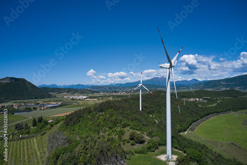 Windmill surrounded by olive trees, vineyards, Alps. Wind turbine in Italy. Wind generators in the mountains of Italy.  Wind farm in the Alpine nature. Wind turbine in Affi, Lake Garda.