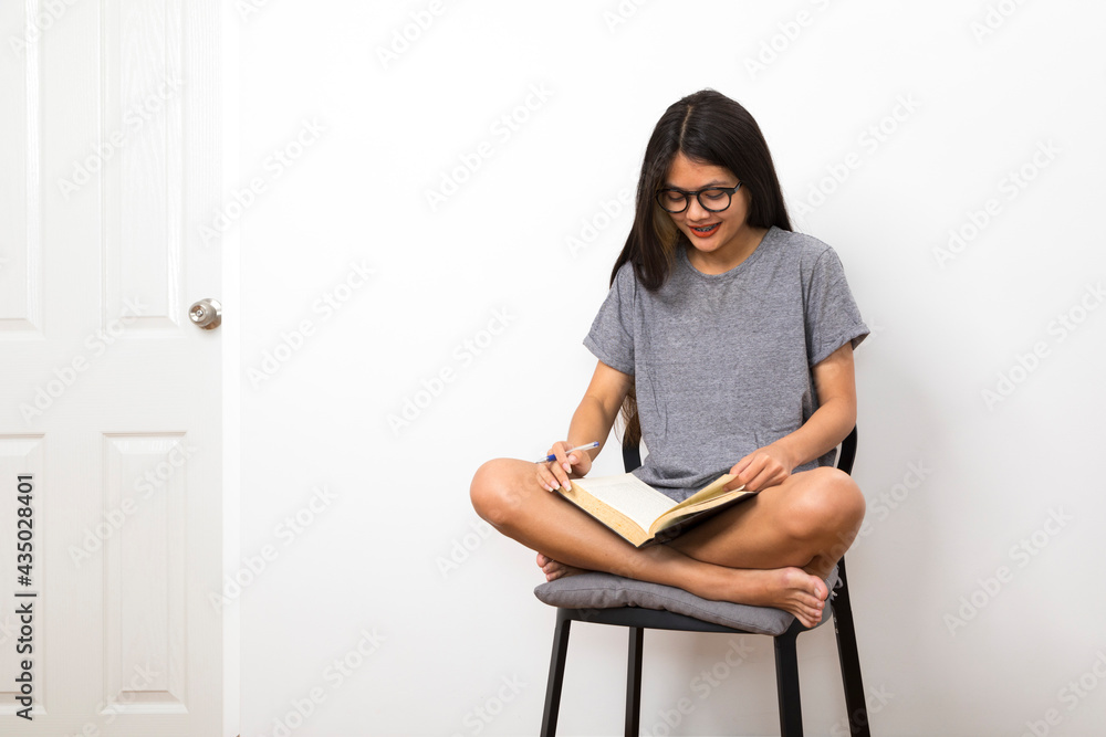 Asian college student sitting on a chair reading a book in her room. Asian college student sitting on a chair reading a book in her room.