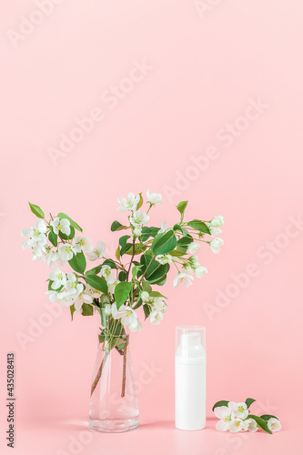 One white blank cosmetic tube bottle and flower  blooming branch on pink background. Natural Organic Spa Cosmetic Beauty Concept. Mockup Front view