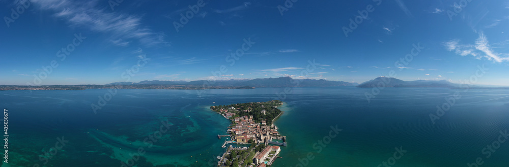 Panorama of Lake Garda. Aerial view of the island of Sirmione. Sirmione, Lake Garda, Italy. Peninsula on a mountain lake in the background of the alps. Castle on the water in Italy.