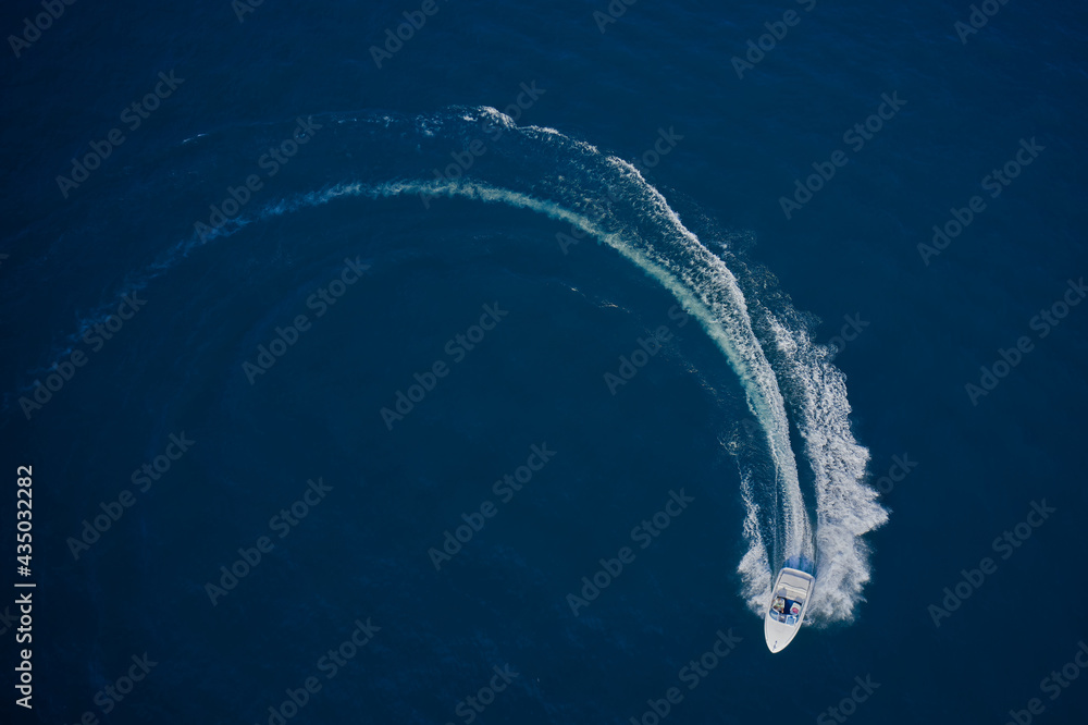 Top view of a white boat sailing in the blue sea. A boat with a motor on blue water in a turn. Top view of the boat. Aerial view luxury motor boat.