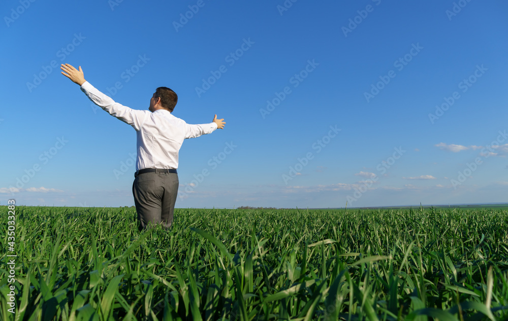businessman poses in a field, he looks into the distance and rests, green grass and blue sky as background businessman poses in a field, he looks into the distance and rests, green grass and blue sky as background