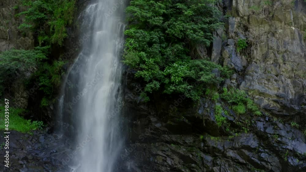 Beautiful landscape with a waterfall in the wild jungle. The drone flies up along the waterfall, you can see bright green trees, gray stones, sprays of the water and lianas Beautiful landscape with a waterfall in the wild jungle. The drone flies up along the waterfall, you can see bright green trees, gray stones, sprays of the water and lianas
