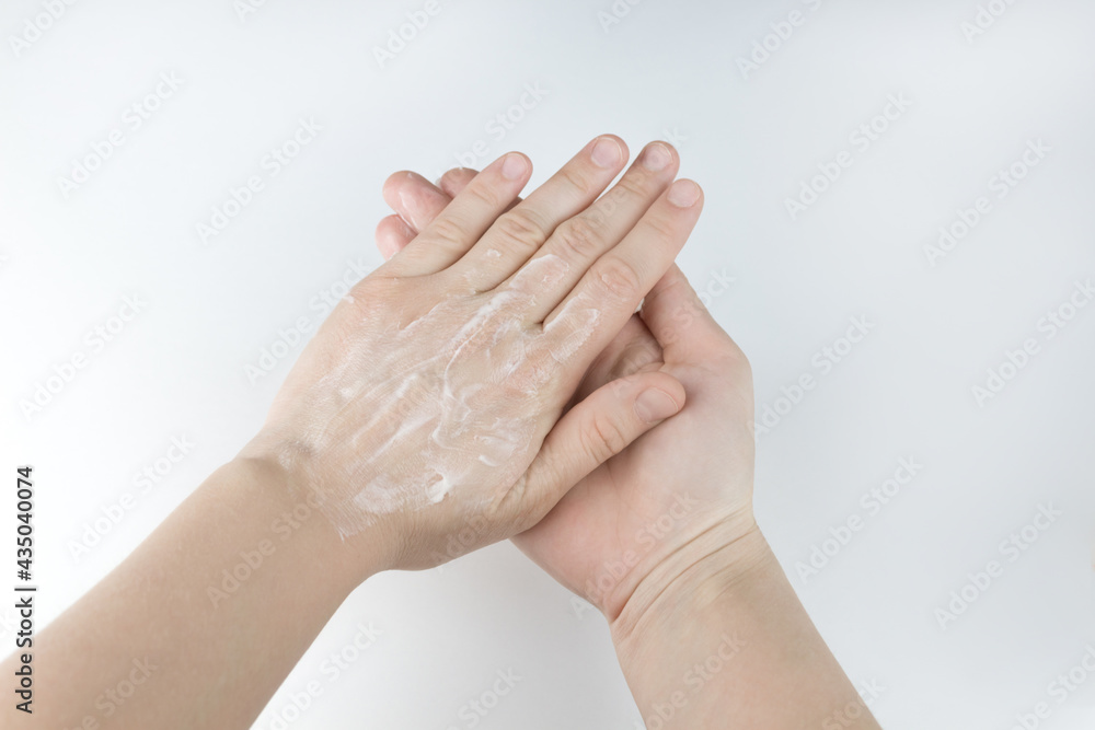 Fototapeta premium Women's hands smear the cream. Hand cream on dry skin. Taking care of yourself. Two hands on a white background.