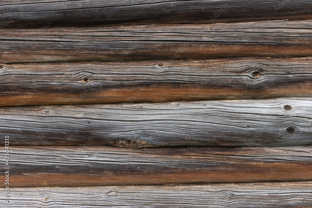 The wall of an old wooden house made of darkened weathered logs. Traditional Russian log hut. The wall of an old wooden house made of darkened weathered logs. Traditional Russian log hut.